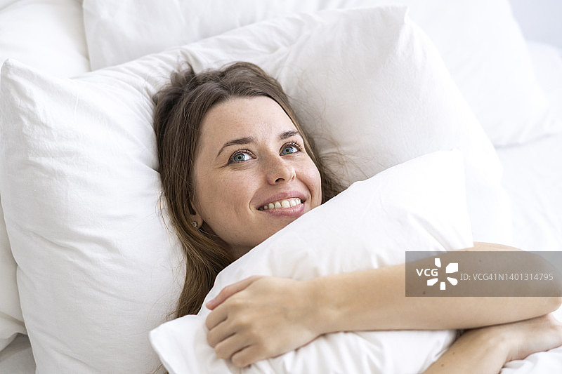 幸福女人抱着枕头躺在床上白日梦在家图片素材
