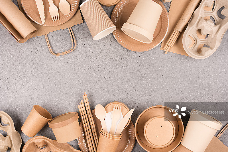 框架由生态纸餐具和用具-纸杯，容器和木制竹制餐具在灰色混凝土背景与复制空间。可持续食品包装理念图片素材