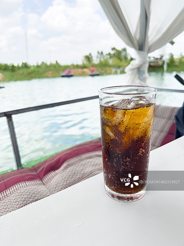在水中间的木筏上放着一张白色的桌子，上面放着一杯软饮和冰块。在炎热的日子里放松身心。泰国，Fizzy water。图片素材