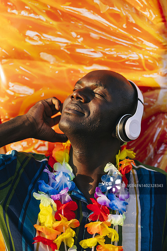 一名非洲男子戴着橙色背景的耳机听音乐图片素材