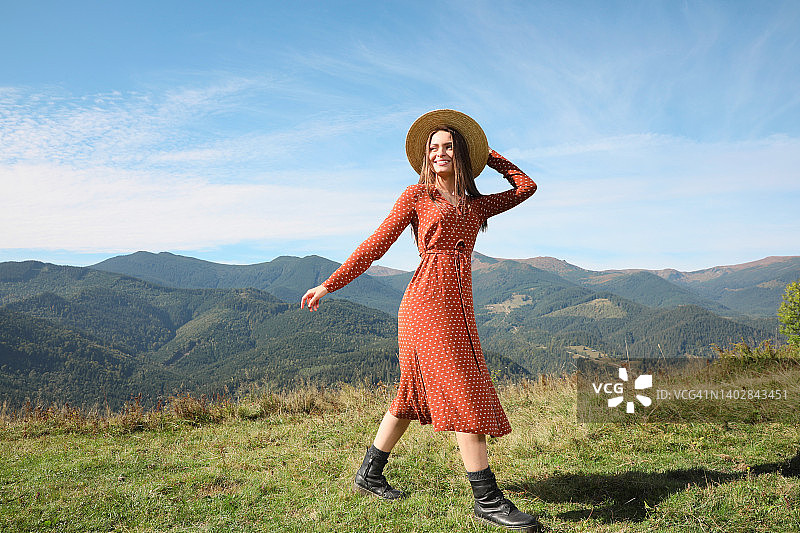 阳光明媚的日子里，戴着草帽的年轻女子走在美丽的山间图片素材