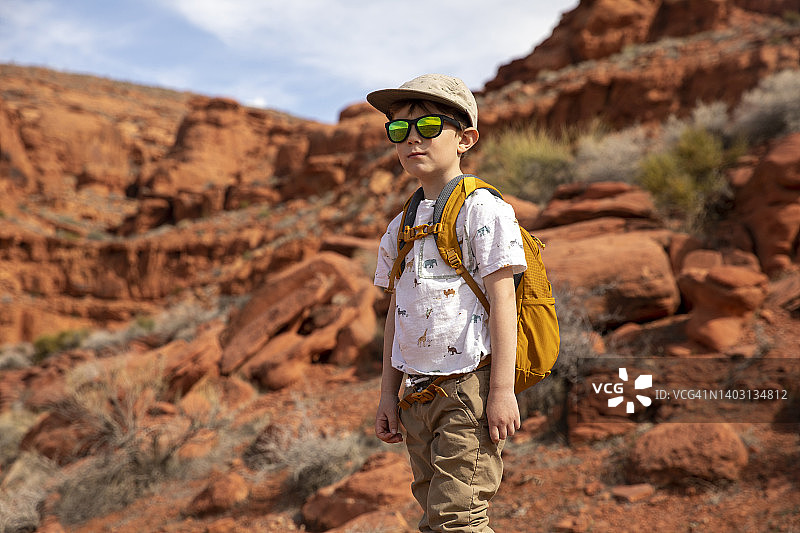 一个戴着墨镜的小男孩沿着一条布满岩石的小径徒步旅行。图片素材