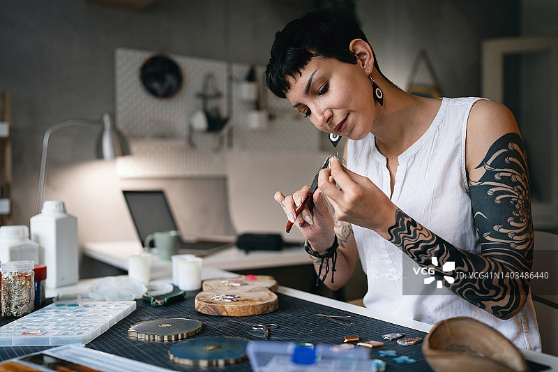 高加索工艺妇女使用钳子在她的车间制造环氧树脂珠宝图片素材