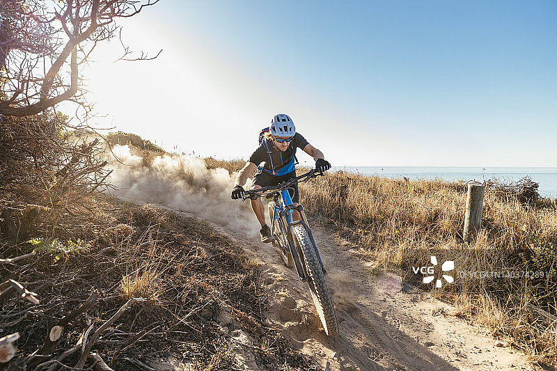 山地自行车手沿着尘土飞扬的小路下山图片素材