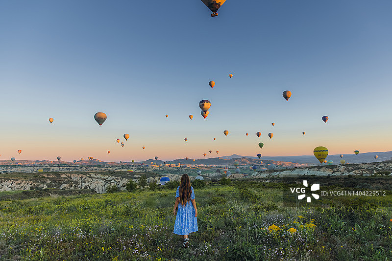 在卡帕多西亚，穿着裙子的快乐女人与热气球在风景优美的山谷迎接日出图片素材