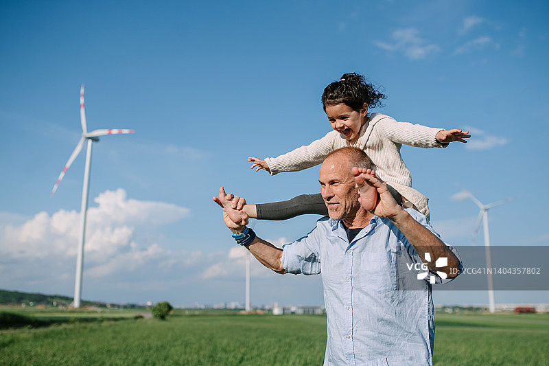父亲和女儿在农田里玩耍，背景是风力发电机。图片素材