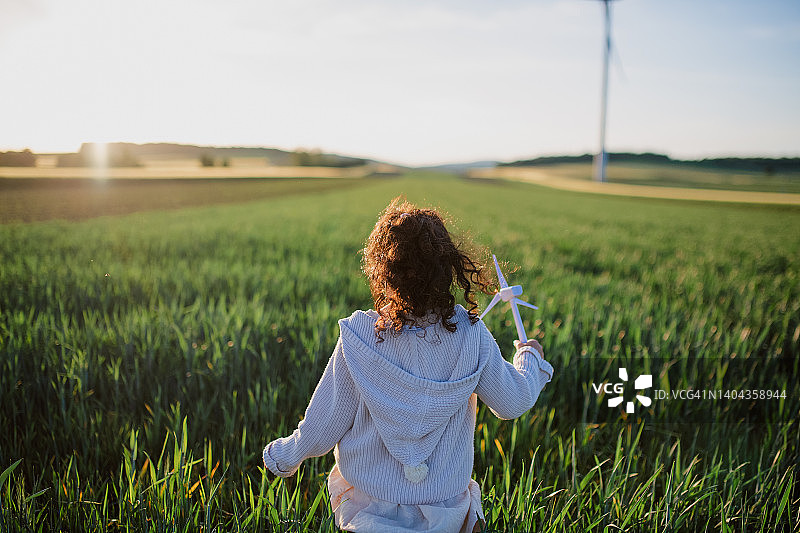 站在野外的小女孩的后视图和风轮机模型。生态未来与可再生资源的概念。图片素材