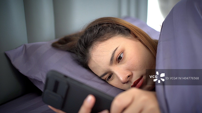 女人用智能手机闹钟睡觉。图片素材