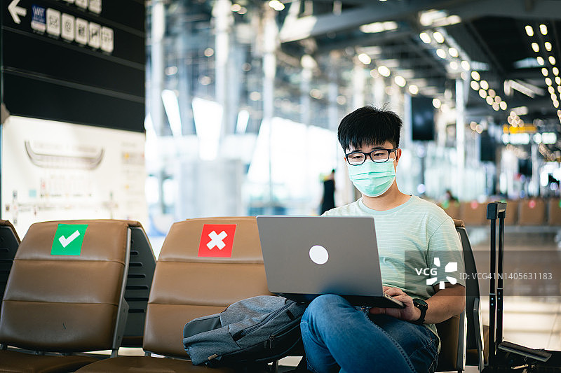 一名戴着口罩用笔记本电脑在机场候机的亚洲青年图片素材