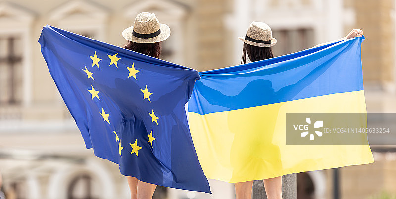 两个朋友的背影，他们举着乌克兰和欧盟的旗帜，在乌克兰的某个城市。图片素材