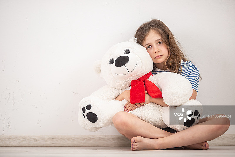 一个患有自闭症的女孩坐在房间的地板上，怀里抱着一只泰迪熊。图片素材