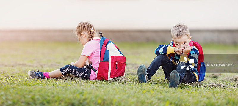 一个男孩和一个女孩背靠背坐在校园的草地上吵架图片素材