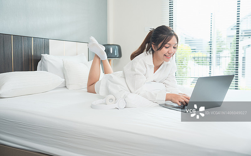 年轻女性躺在床上使用笔记本电脑。年轻女子躺在床上用笔记本电脑打字工作。远程学习。自由职业者。在家里工作。在线教育图片素材