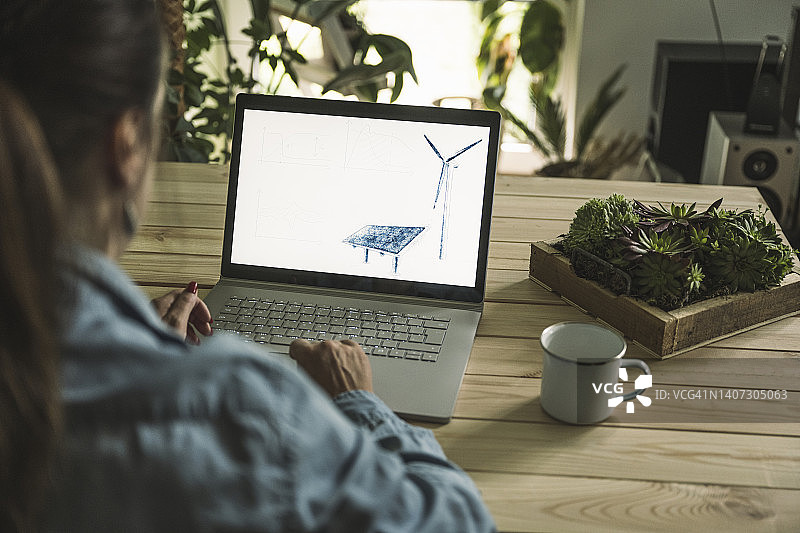 自由职业者，在家庭办公室的笔记本电脑屏幕上绘制太阳能电池板和风力涡轮机的草图图片素材