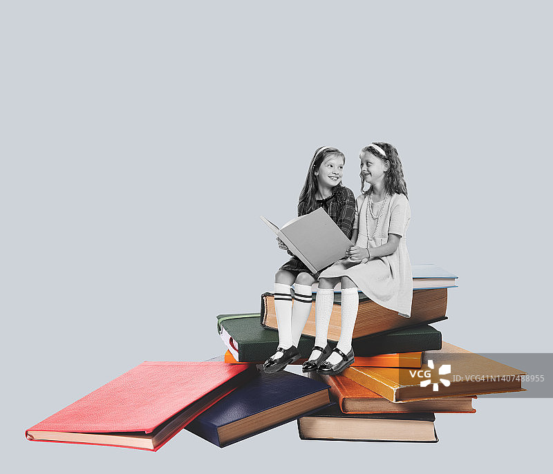 当代艺术拼贴。两个漂亮的女孩，孩子们坐在书本上，隔着灰色的背景阅读图片素材