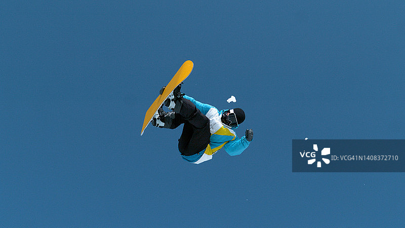 从下往上:年轻的男性单板滑雪运动员在空中做一个旋转动作。图片素材
