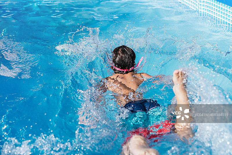 在一个可移动的小游泳池的房子里玩耍的不知名的孩子的后视图。孩子在水里游泳。图片素材