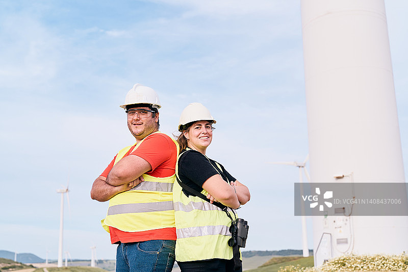 年轻的电气工程师男女交叉双臂站在风力涡轮机前图片素材