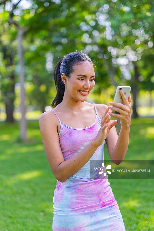一个美丽的和好看的年轻亚洲女性模特女士穿着五颜六色的夏天冷连衣裙在公园的手机图片素材