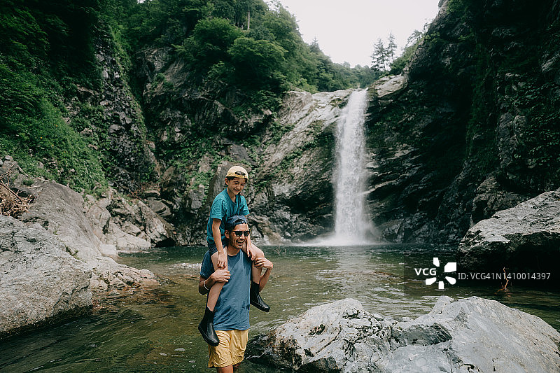 父亲扛着孩子走在瀑布前图片素材