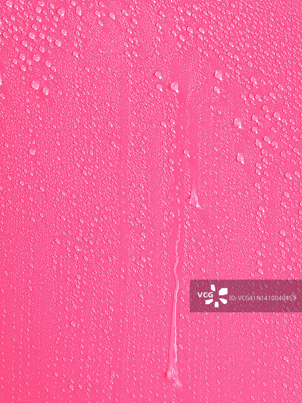 雨滴在粉红色的背景上滑动。图片素材