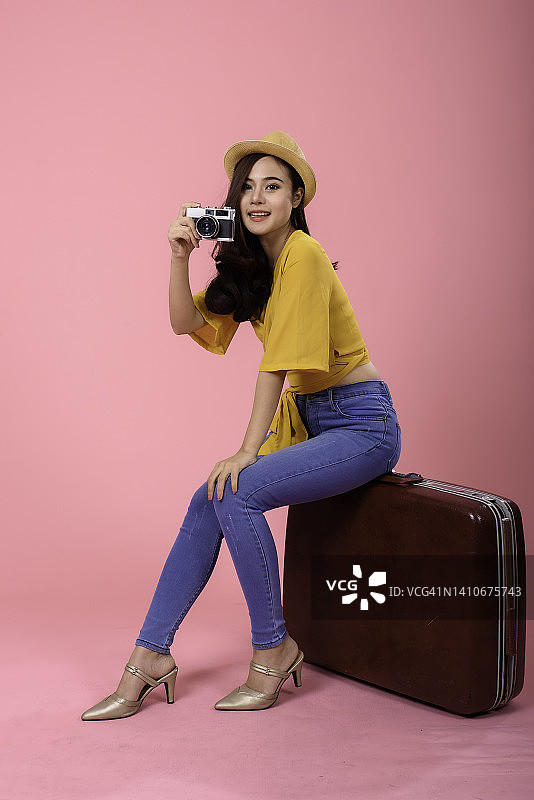 旅行者旅游年轻的亚洲妇女在夏天站在拿着相机的粉红色背景。图片素材