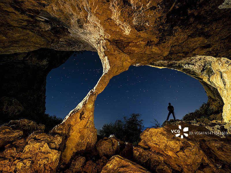 一个人的剪影从一个大山洞里凝视夜空。图片素材
