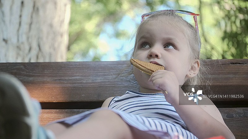 小女孩吃姜饼。特写的金发女孩坐在公园的长凳上吃饼干。图片素材