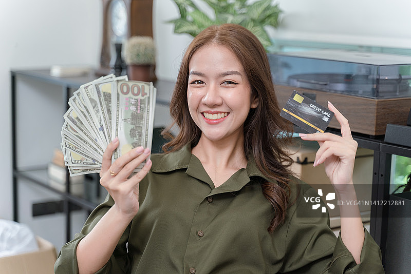 一位快乐的年轻女士拿着信用卡和钞票。准备好体验一次购物狂欢。图片素材
