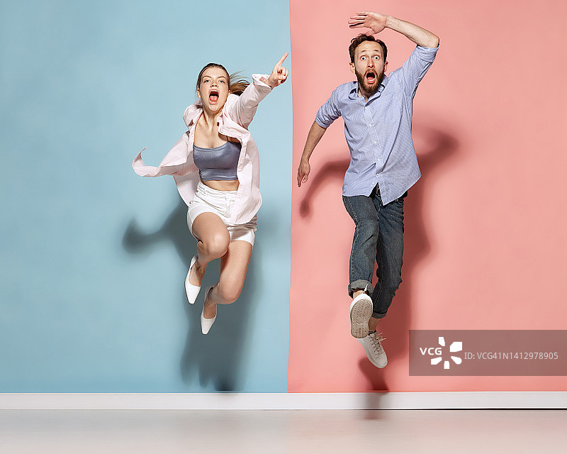惊讶的男女在蓝色和粉色的背景上奔跑跳跃。人类的情感、青春、爱和积极的生活方式理念图片素材