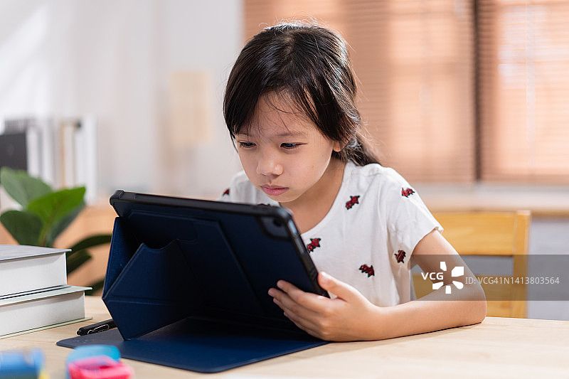小亚洲学生女孩试着在家里在线学习的同时专注于看书作为一种近视的预防图片素材
