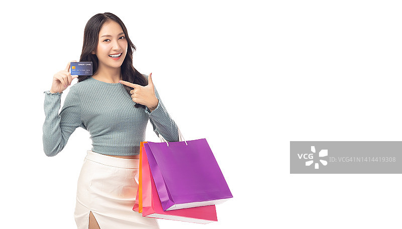 时髦的年轻亚洲女性持有塑料信用卡和购物袋指向信用卡美丽的购物女孩指向信用卡微笑看着相机孤立的白色背景图片素材