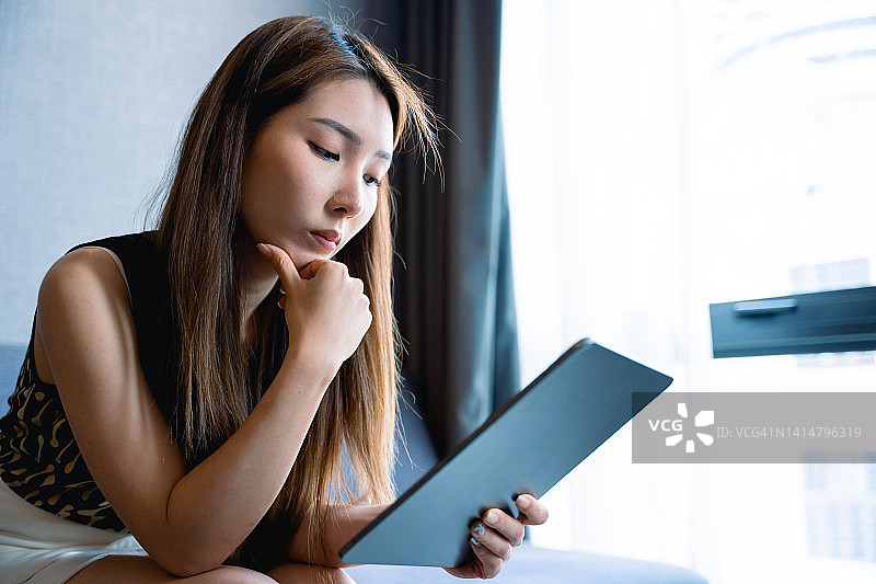 一位亚洲女性在酒店房间里坐在沙发上使用电子平板电脑图片素材