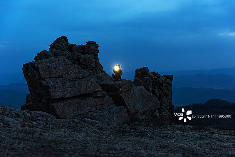 中国梁丙山，一名女摄影师晚上坐在一块巨石上图片素材