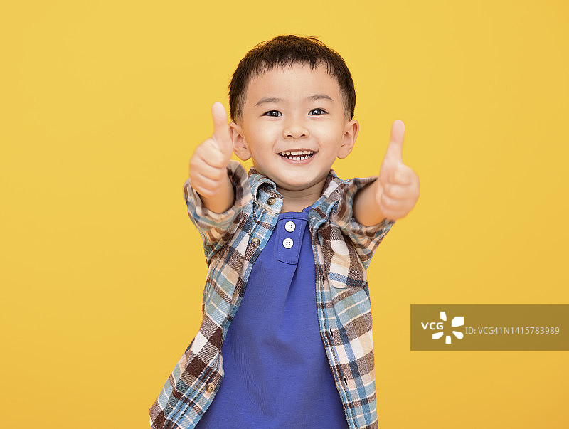 快乐的小男孩在黄色背景前竖起大拇指图片素材