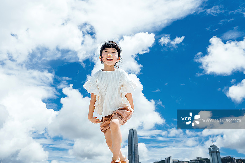 在维多利亚港的海滨长廊上，亚洲小女孩在美丽的蓝天下翩翩起舞。在一个阳光明媚的日子里在城市的户外玩得很开心图片素材