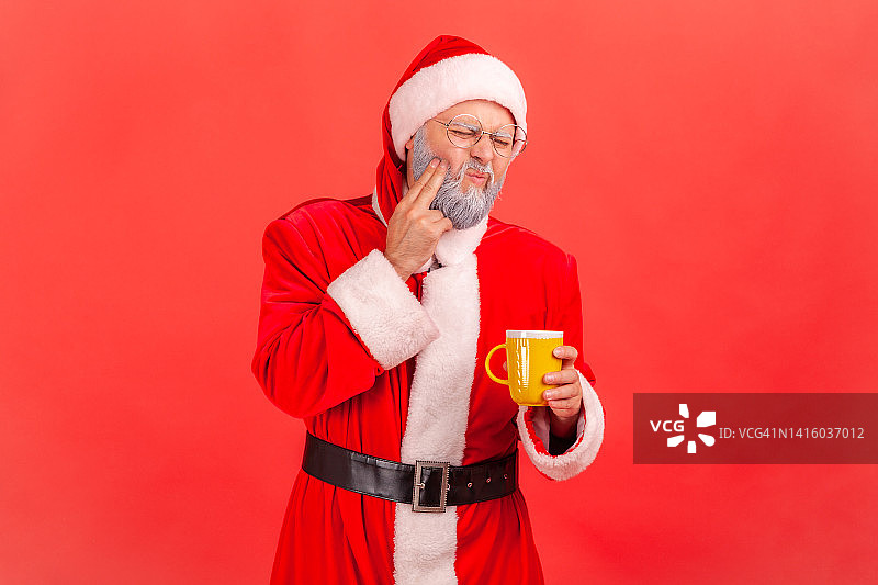 一名身穿圣诞老人服装、胡子花白的老人在喝了冷热饮料后牙齿疼痛。图片素材