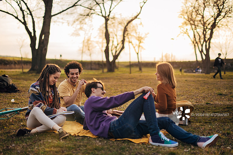 一群来自不同种族的朋友坐在公园里的黄色野餐毯子上闲逛图片素材