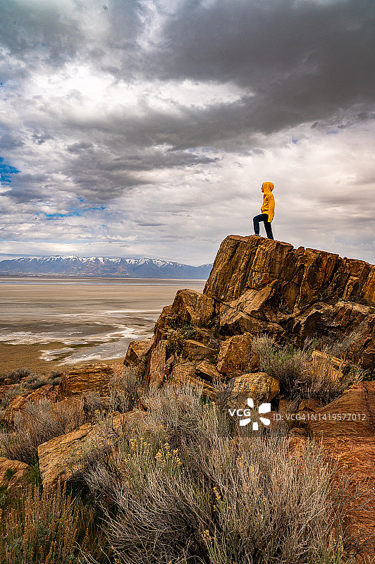 犹他州，一个男孩站在一块高高的岩石上俯瞰着干涸的湖床图片素材