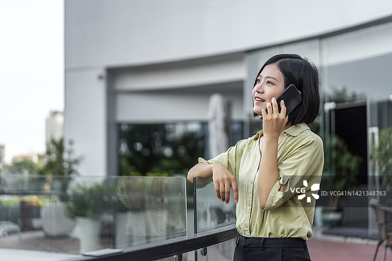 自信的年轻亚洲女商人站在城市阳台上使用智能手机图片素材