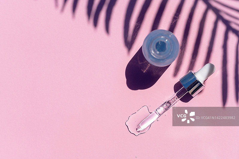 透明玻璃瓶与蓝色美容精华水疗护理在粉红色的背景。图片素材