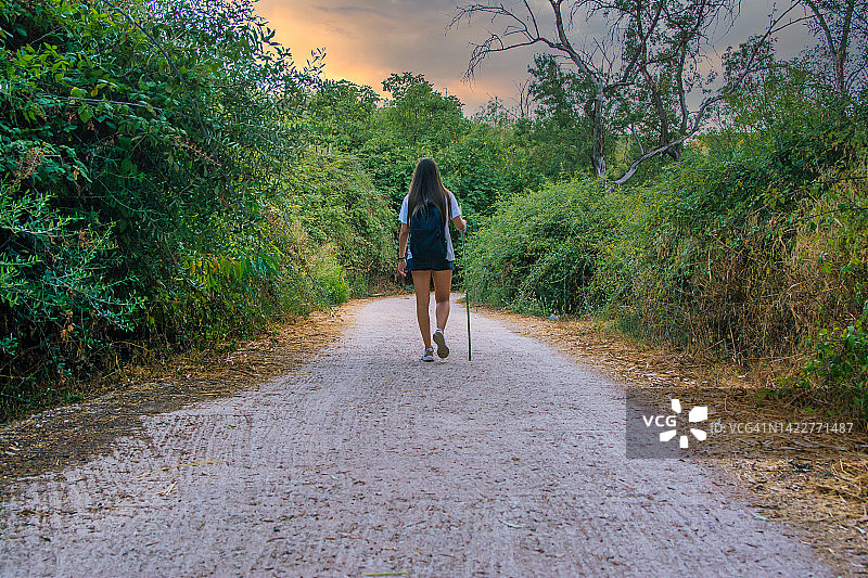 一个女孩走在乡间的徒步小道上的后视图。图片素材