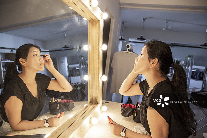 亚洲妇女在木制灯泡镜前化妆睫毛图片素材
