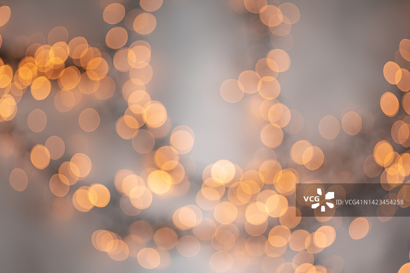 象征即将到来的圣诞节和新年的节日彩灯。灰色背景上有许多明亮的橙色照明散景。你的设计背景图片素材