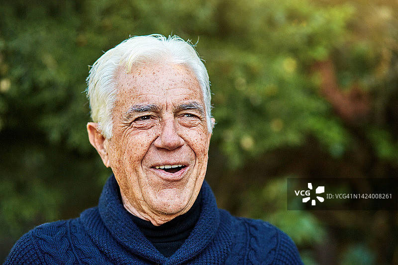一位白发苍苍的老人站在枝繁叶茂的花园里，开心地笑着图片素材