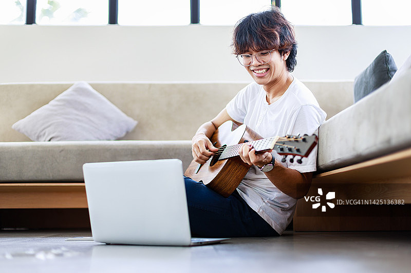 年轻人演奏着原声吉他，坐在家里的地板上图片素材