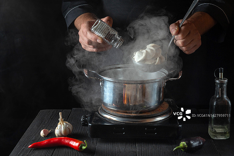 厨师在餐厅厨房用平底锅煮饺子。特写的厨师加盐的手。免费的广告空间。图片素材