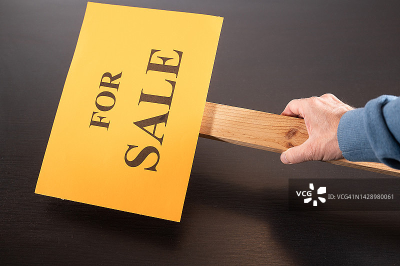 卖房子的概念。一个人从桌子上拿起一张海报，上面写着:“出售”。图片素材