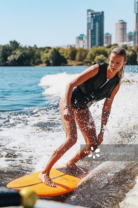 年轻美丽的女子训练Wake冲浪对城市景观背景图片素材