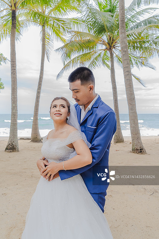 新郎和新娘在海滩上，背景是许多椰子树和大海。图片素材